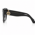 Lentes de sol Gucci negros en vista lateral, con patilla ancha, logo GG dorado y montura brillante sobre fondo blanco.