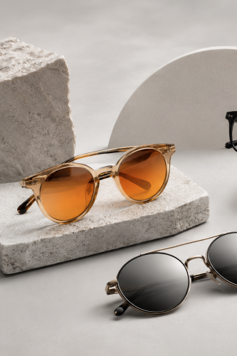 Composición moderna de lentes ópticos y lentes de sol premium sobre fondo gris claro, con cristales de tonos cálidos y estilo elegante para tienda Maaig.